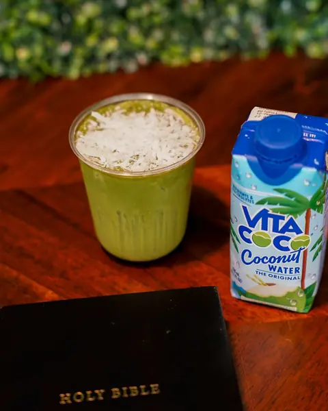 Matcha nube de coco con coco rallado encima, junto a un cartón de agua de coco y una Biblia.