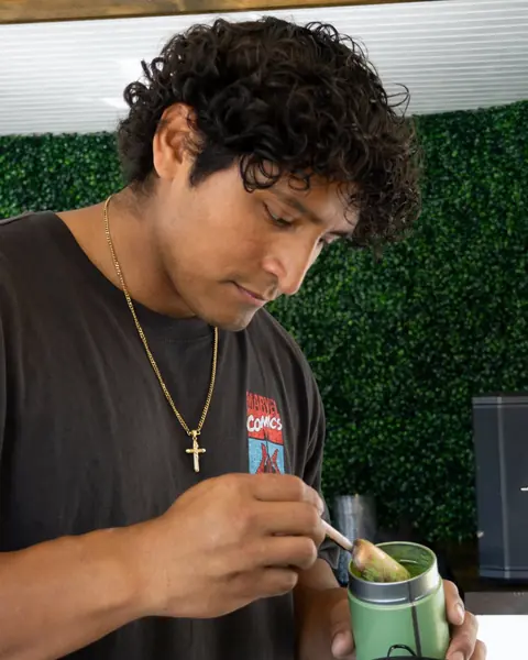 El fundador Erick Claure echando matcha en polvo en un colador sobre un tazón dentro del tráiler de Primero Dios Matcha.