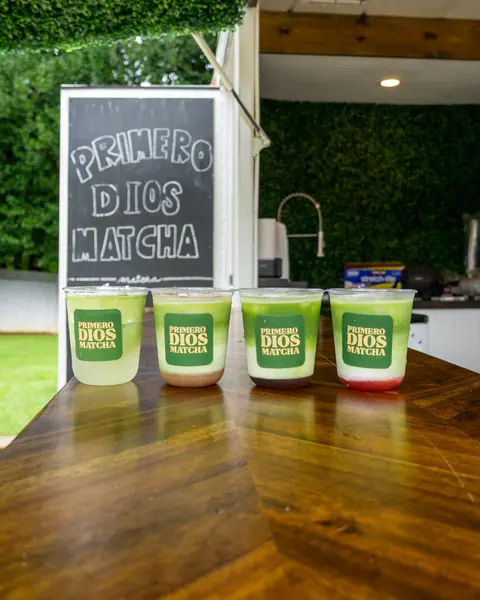 Cuatro bebidas de Primero Dios Matcha en fila sobre el mostrador de madera del tráiler, frente a una pizarra.